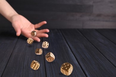 Woman throwing gold dice on black wooden table, closeup. Space for text