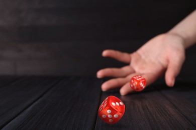 Image of Woman throwing red dice on black wooden table, closeup. Space for text