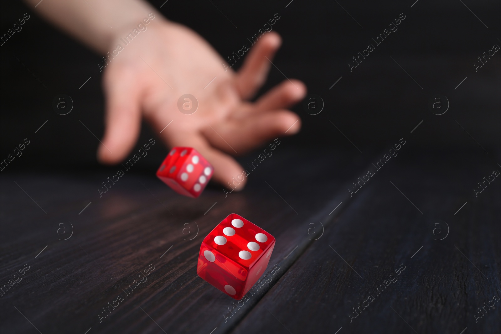 Image of Woman throwing red dice on black wooden table, closeup. Space for text