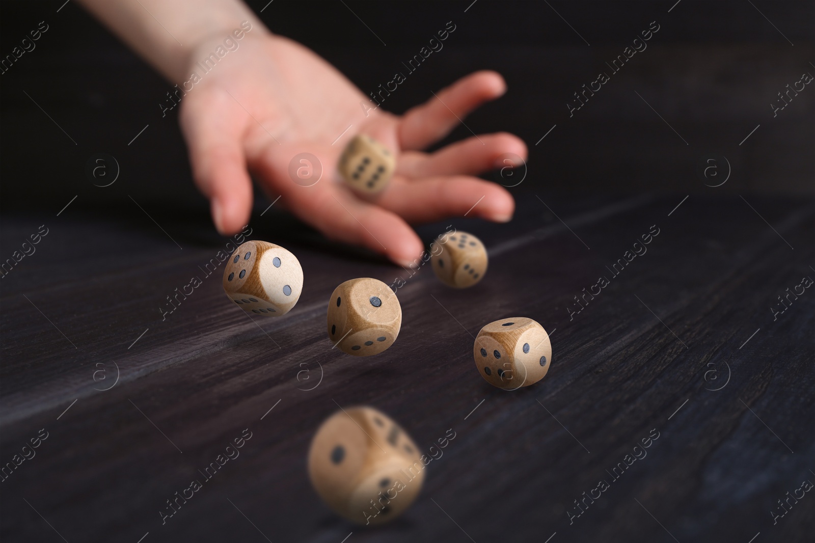 Image of Woman throwing wooden dice on black table, closeup. Space for text