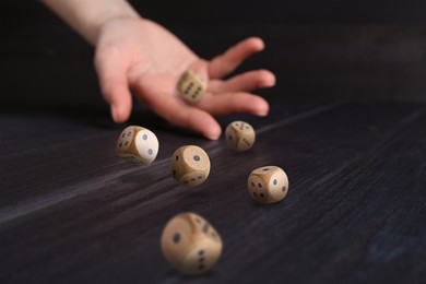 Image of Woman throwing wooden dice on black table, closeup. Space for text