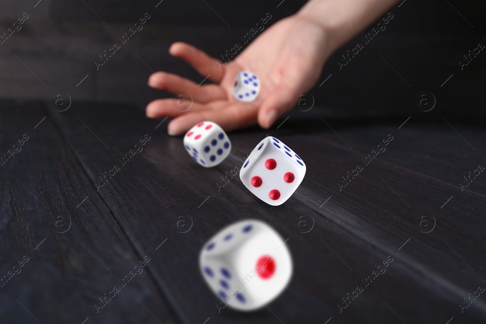 Image of Woman throwing white dice on black wooden table, closeup