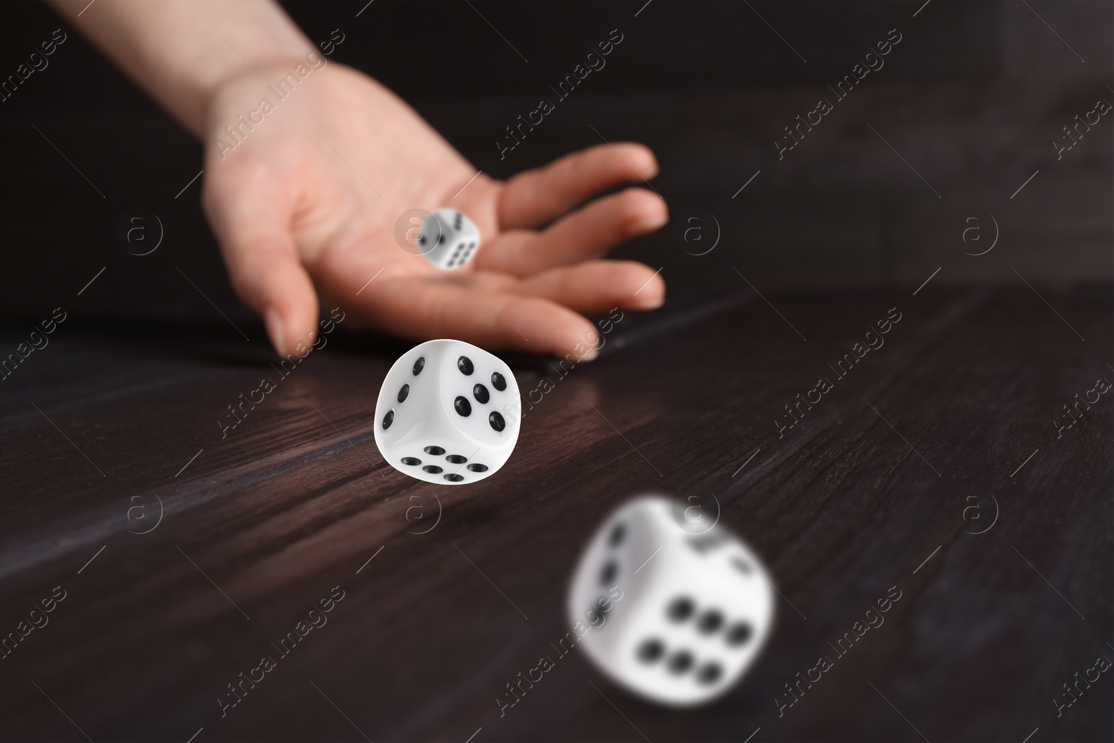 Image of Woman throwing white dice on wooden table, closeup. Space for text