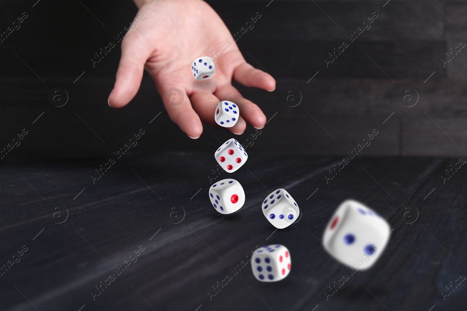 Image of Woman throwing white dice on black wooden table, closeup