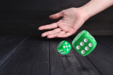 Image of Woman throwing green dice on black wooden table, closeup. Space for text