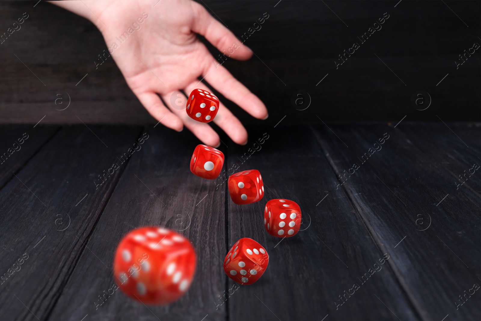 Image of Woman throwing red dice on black wooden table, closeup. Space for text