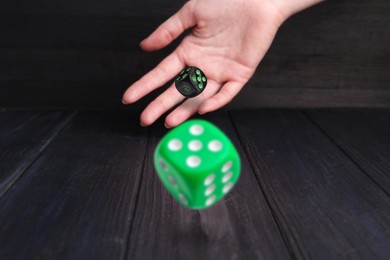 Image of Woman throwing dice on black wooden table, closeup