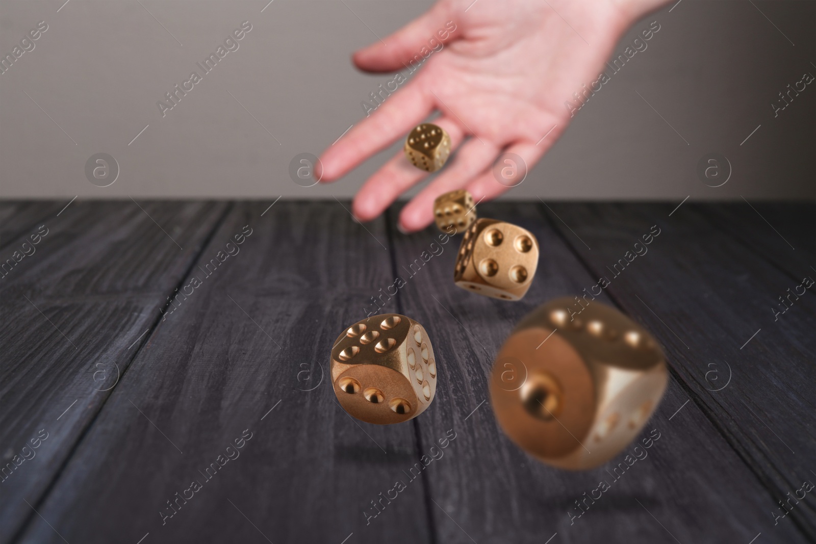 Image of Woman throwing gold dice on black wooden table, closeup. Space for text