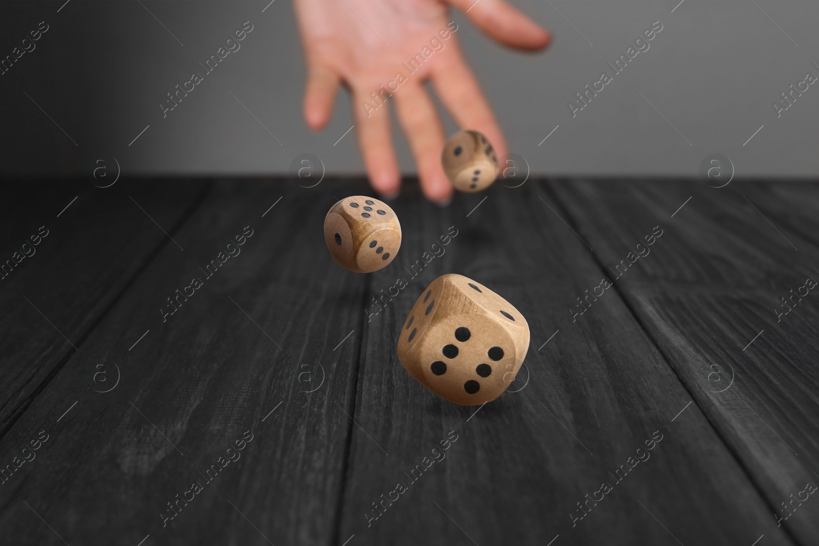 Image of Woman throwing dice on black wooden table, closeup