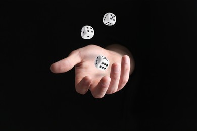 Image of Man throwing white dice in darkness, closeup