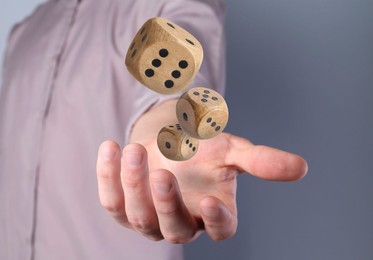 Image of Man throwing wooden dice on grey background, closeup. Space for text