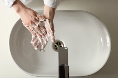 Photo of Woman washing hands with cleansing foam near sink in bathroom, top view