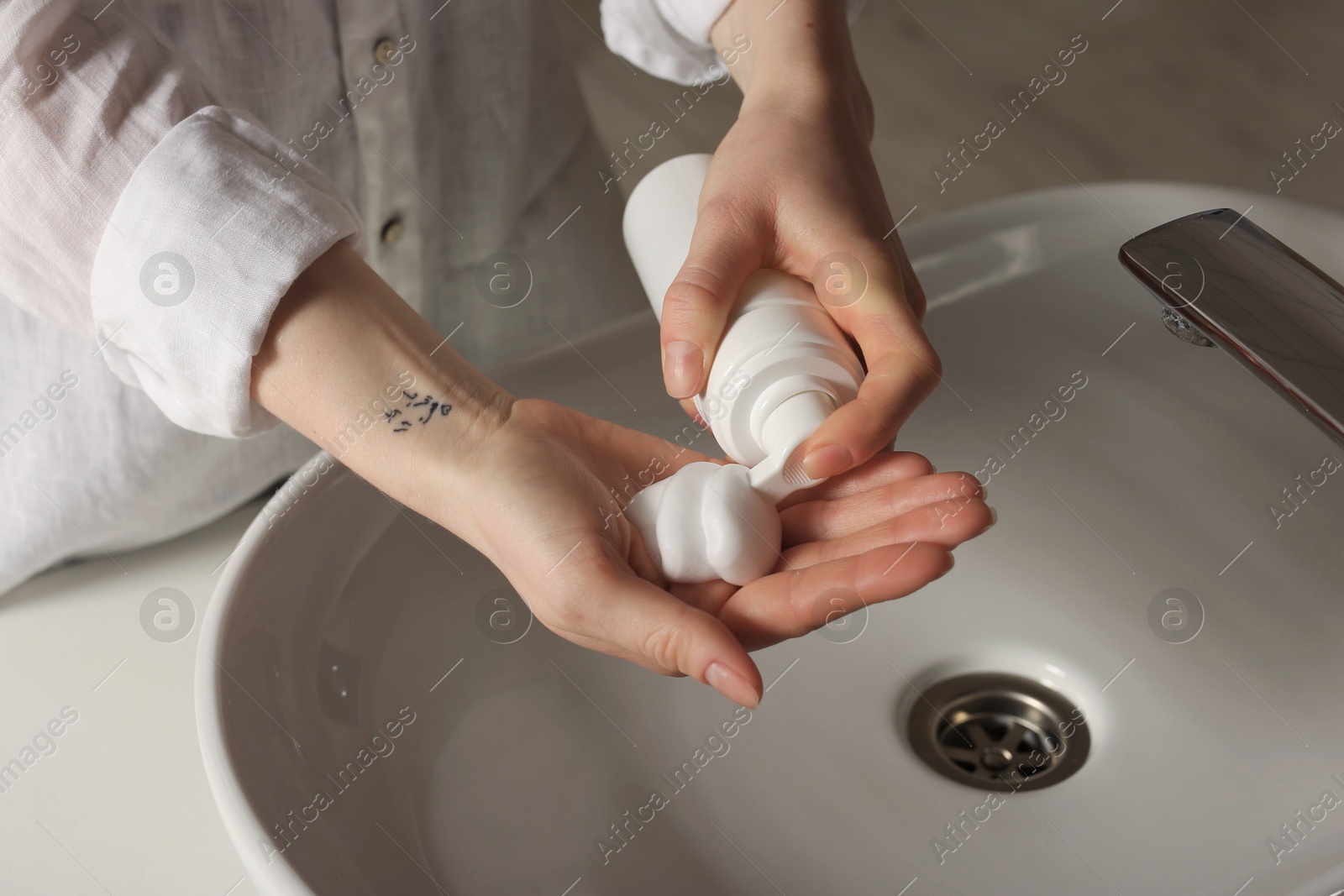 Photo of Woman washing hands with cleansing foam near sink in bathroom, closeup