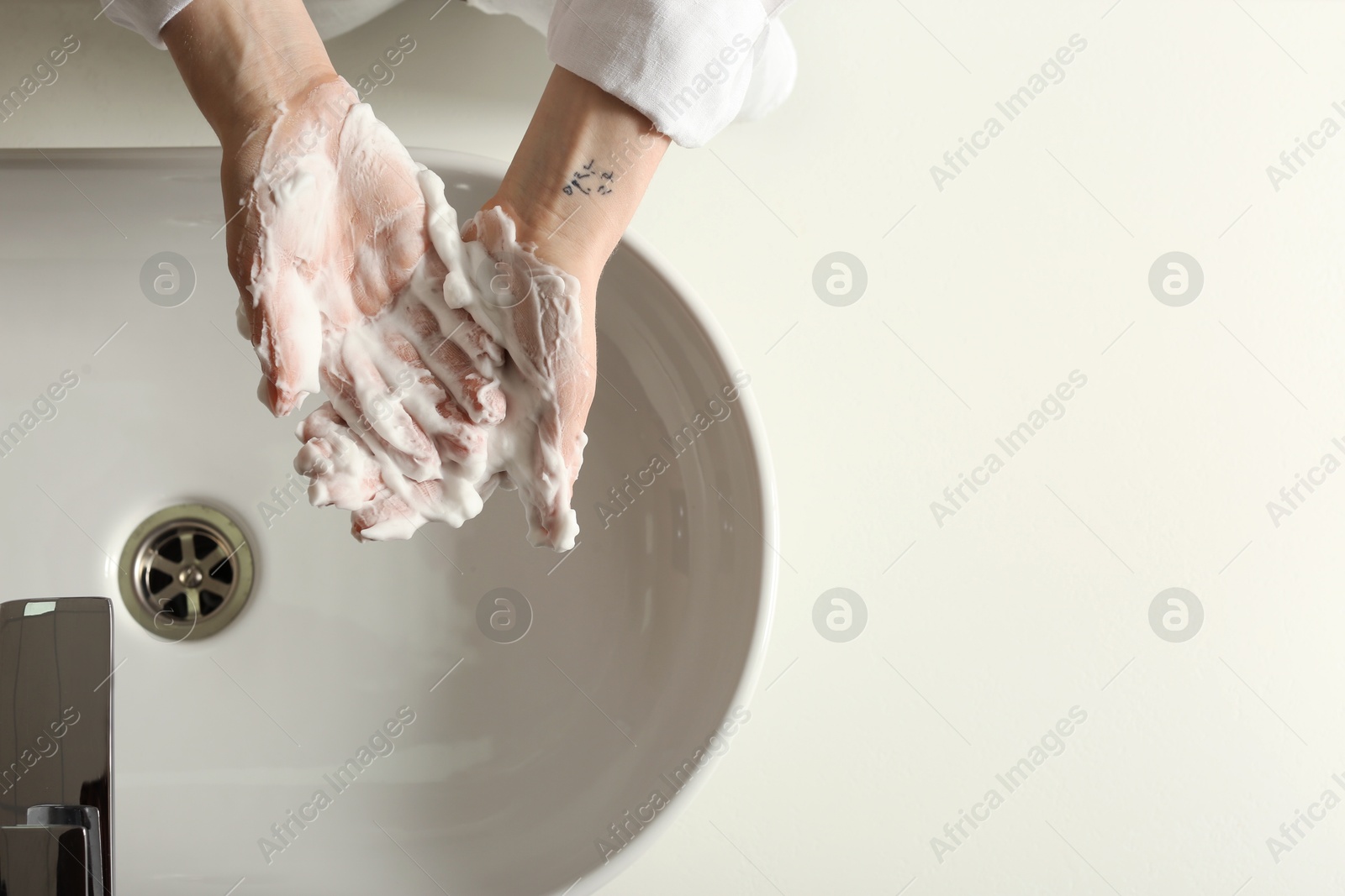 Photo of Woman washing hands with cleansing foam near sink in bathroom, top view. Space for text