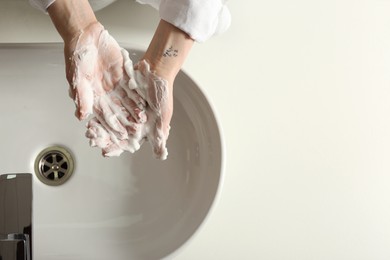 Photo of Woman washing hands with cleansing foam near sink in bathroom, top view. Space for text