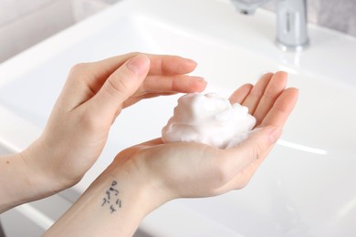 Photo of Woman washing hands with cleansing foam near sink in bathroom, closeup