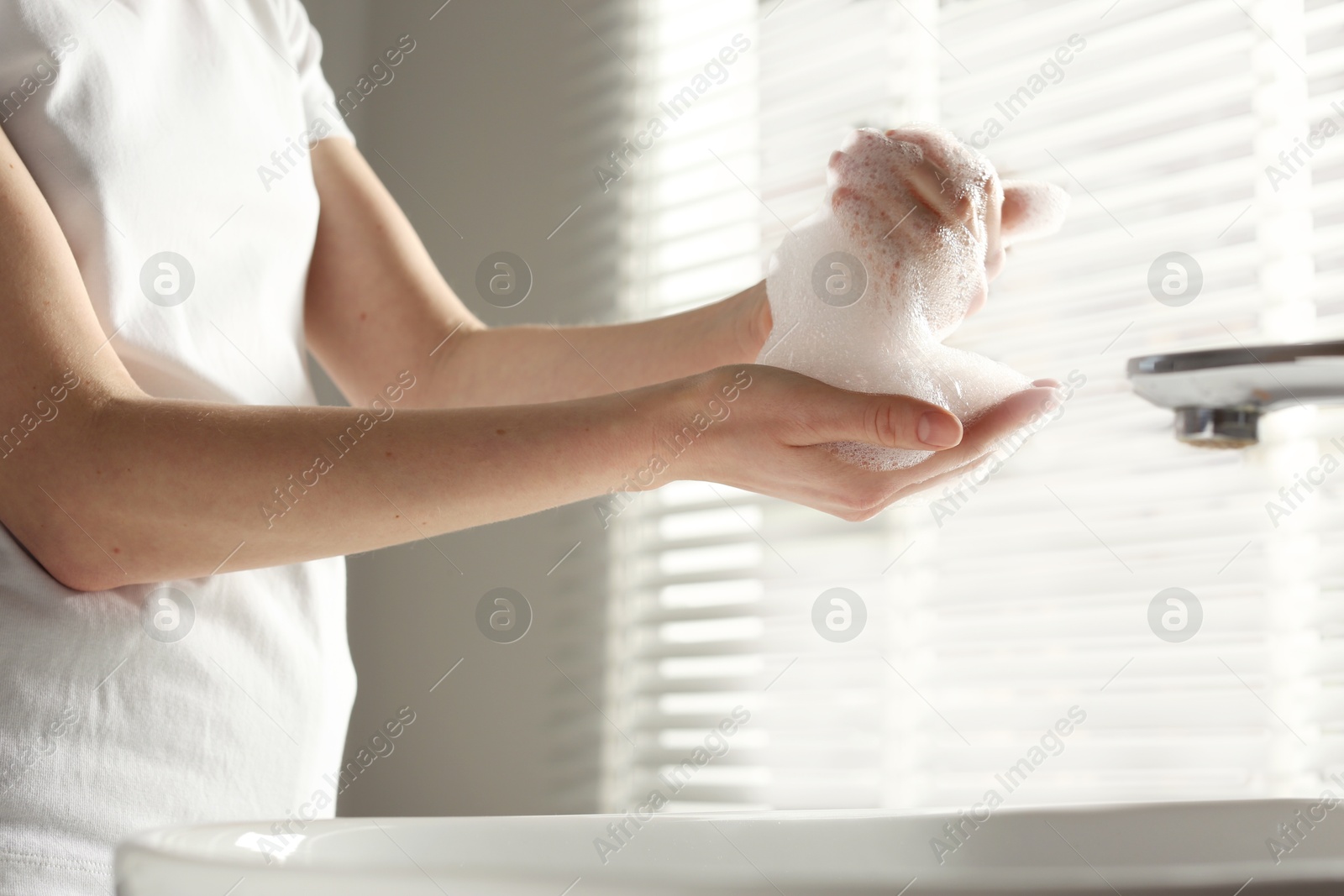 Photo of Woman washing hands with cleansing foam near sink in bathroom, closeup