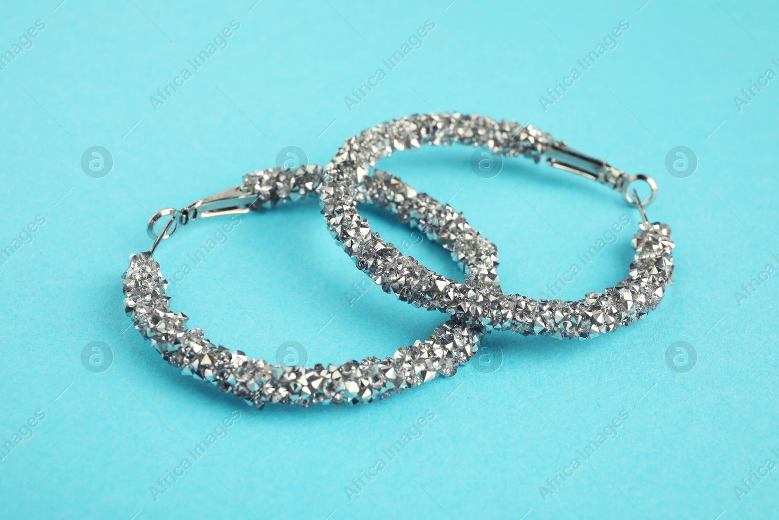 Photo of Beautiful bijouterie. Elegant earrings on light blue background, closeup