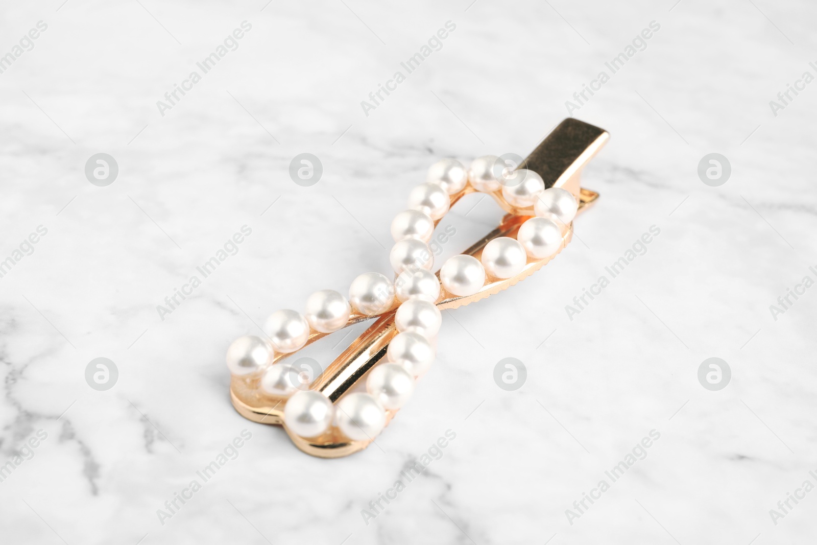 Photo of Beautiful bijouterie. Elegant hair clip on white marble table, closeup