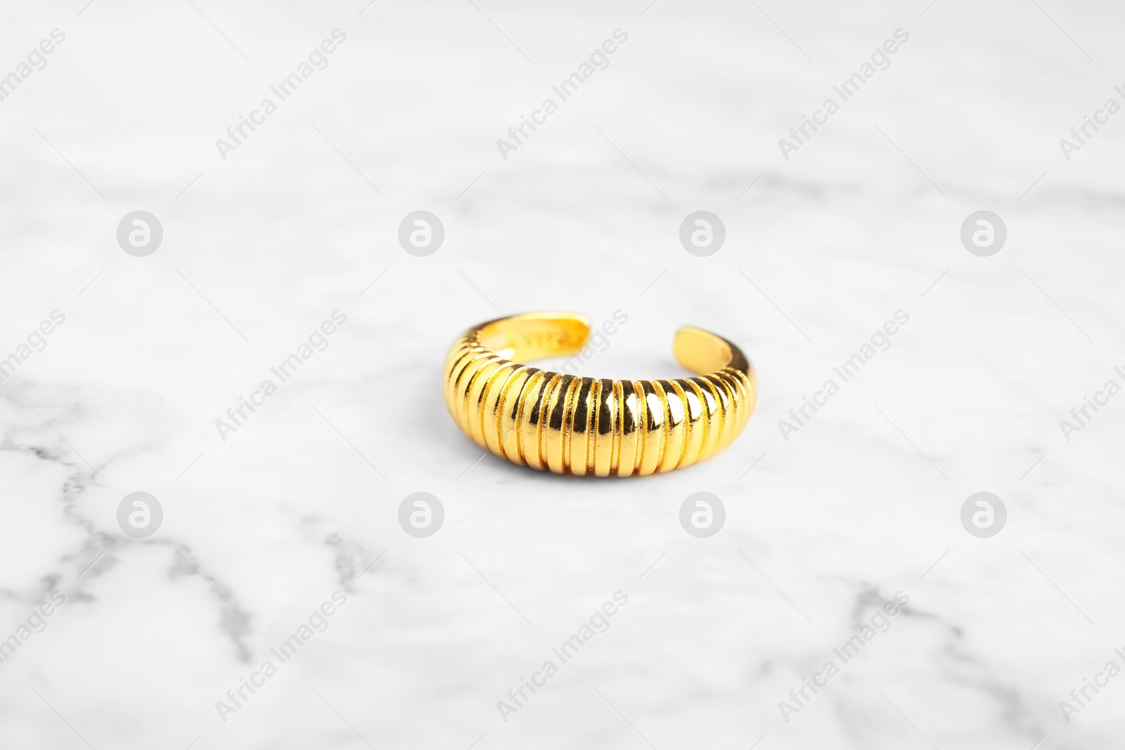 Photo of Beautiful bijouterie. Stylish ring on white marble table, closeup