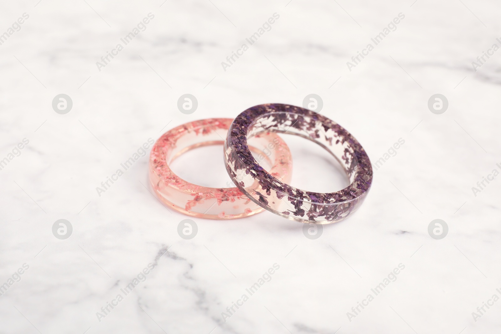 Photo of Beautiful bijouterie. Stylish rings on white marble table, closeup