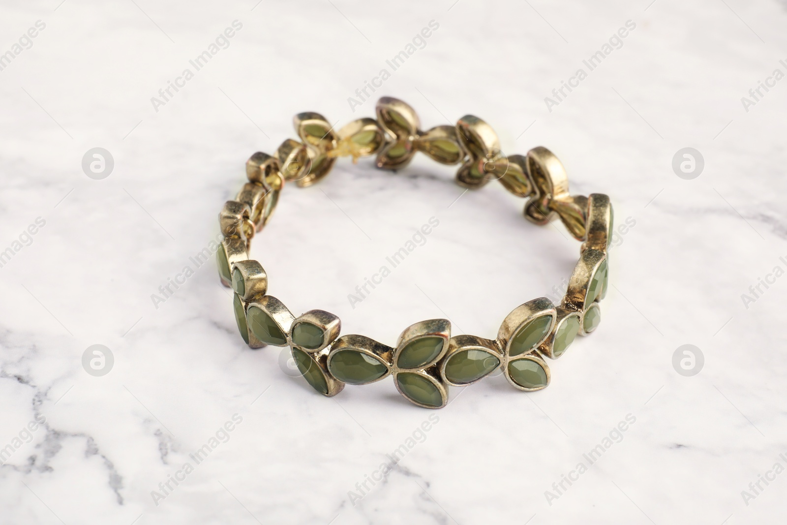 Photo of Beautiful bijouterie. Stylish bracelet on white marble table, closeup