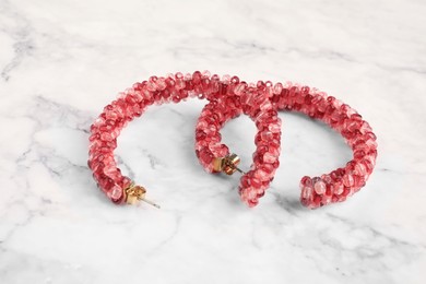 Photo of Beautiful bijouterie. Stylish earrings on white marble table, closeup