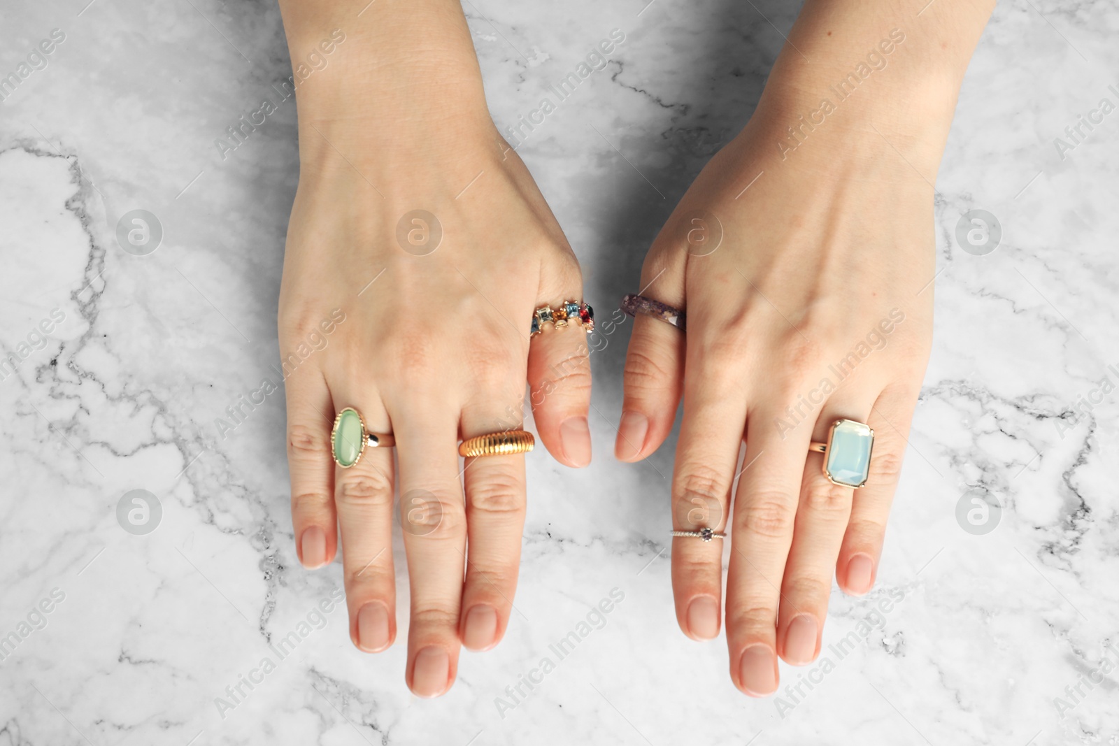 Photo of Beautiful bijouterie. Woman wearing different stylish rings at white marble table, top view