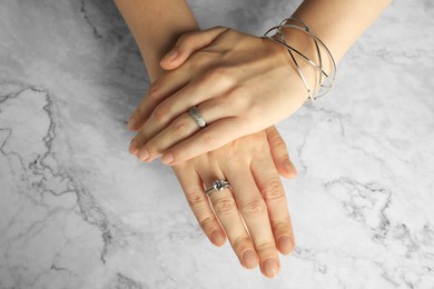 Photo of Beautiful bijouterie. Woman wearing different stylish rings and bracelet at white marble table, top view