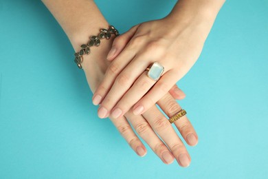 Photo of Beautiful bijouterie. Woman wearing different stylish rings and bracelet on light blue background, top view