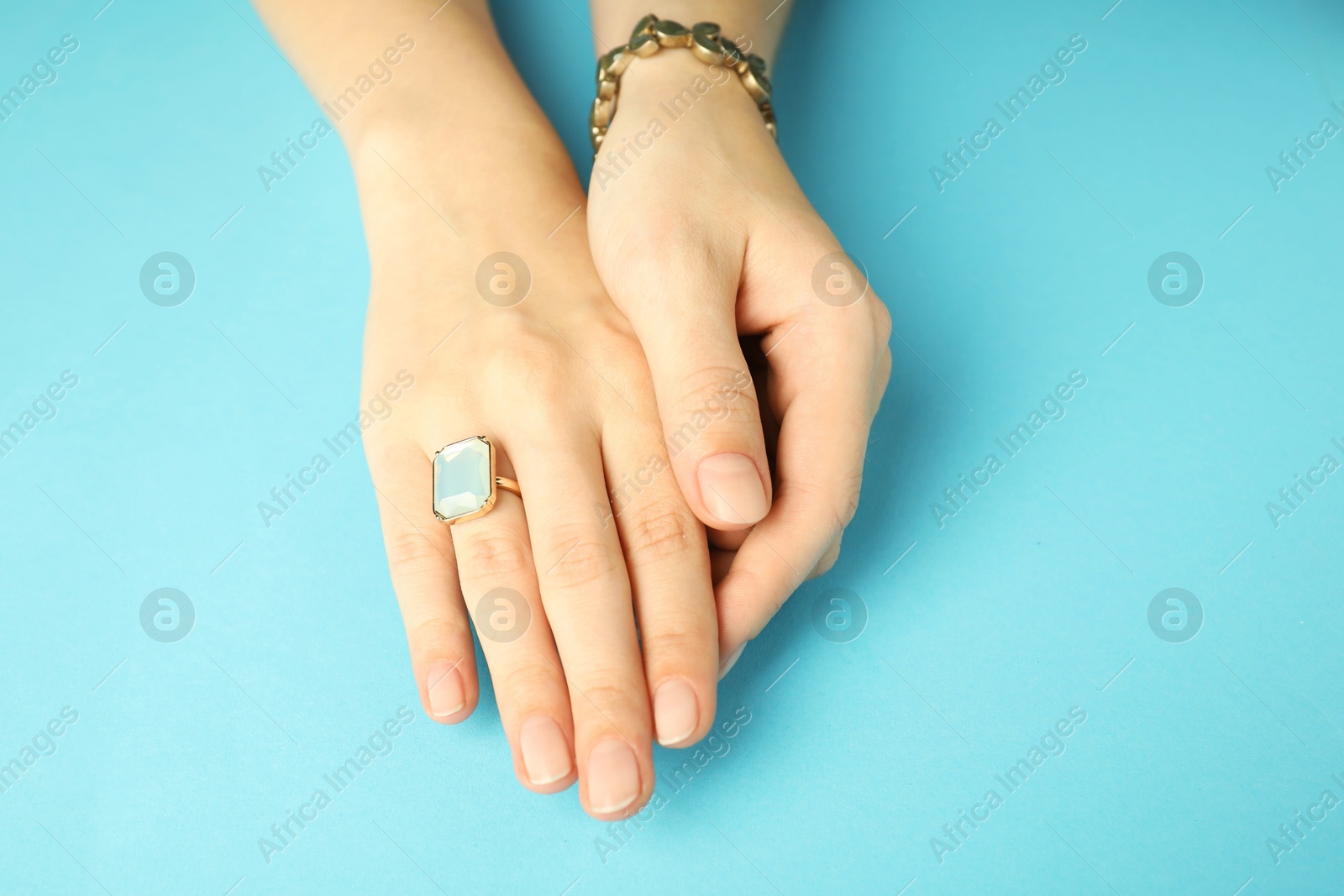 Photo of Beautiful bijouterie. Woman wearing stylish ring and bracelet on light blue background, closeup