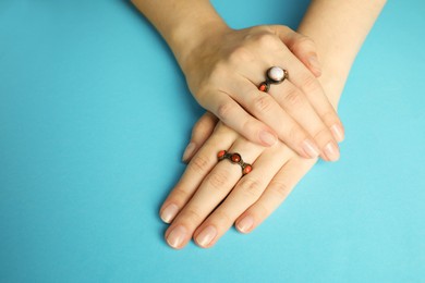 Photo of Beautiful bijouterie. Woman wearing stylish rings on light blue background, closeup