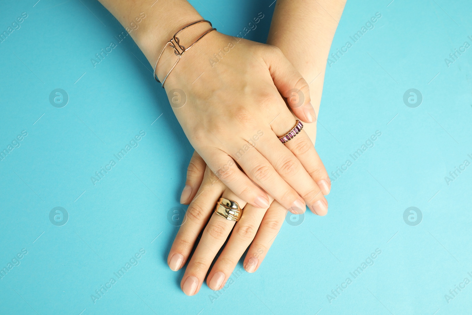 Photo of Beautiful bijouterie. Woman wearing stylish rings and bracelet on light blue background, top view