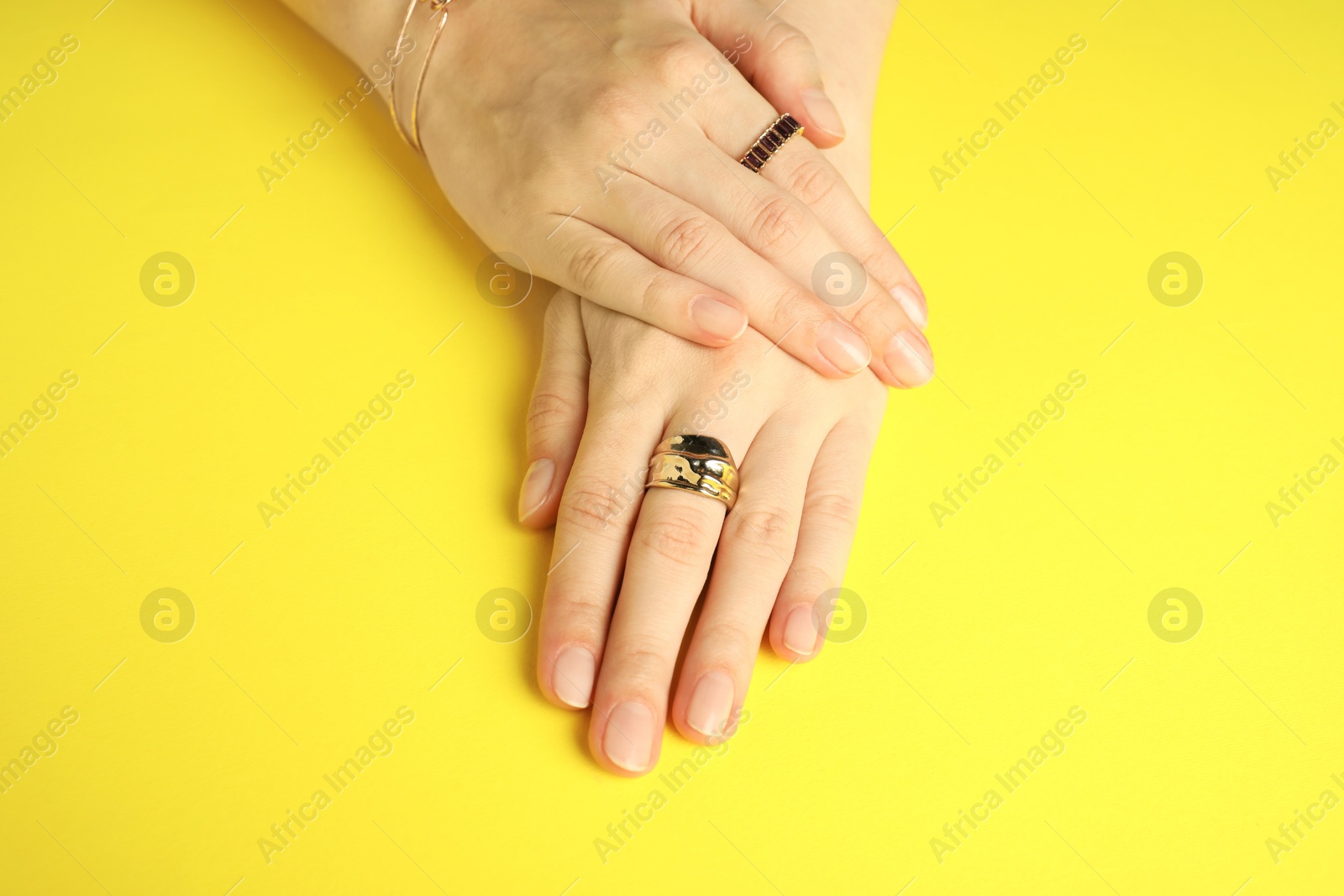 Photo of Beautiful bijouterie. Woman wearing different stylish rings and bracelet on yellow background, closeup