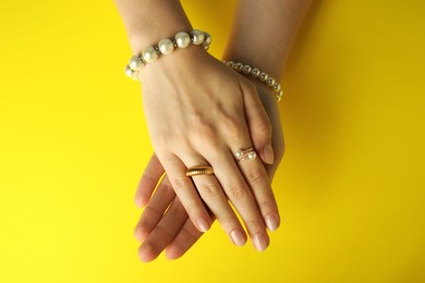 Photo of Beautiful bijouterie. Woman wearing different stylish rings and bracelets on yellow background, top view