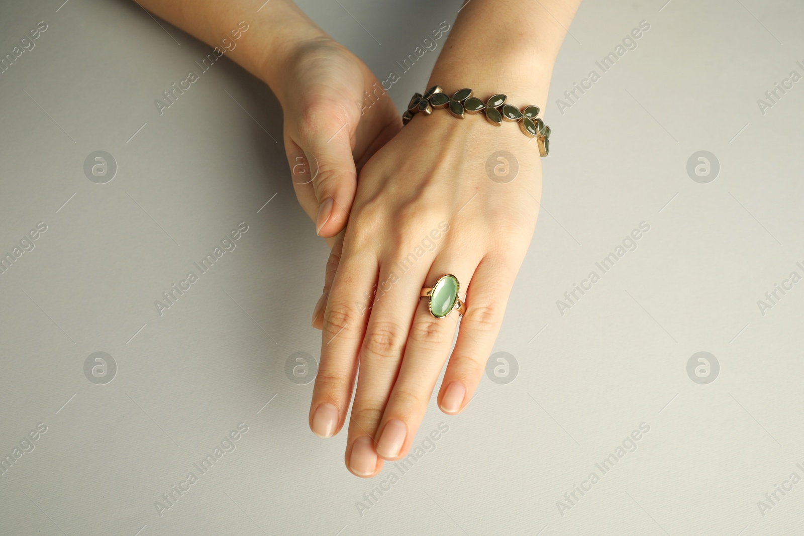 Photo of Beautiful bijouterie. Woman wearing stylish ring and bracelet on light grey background, closeup