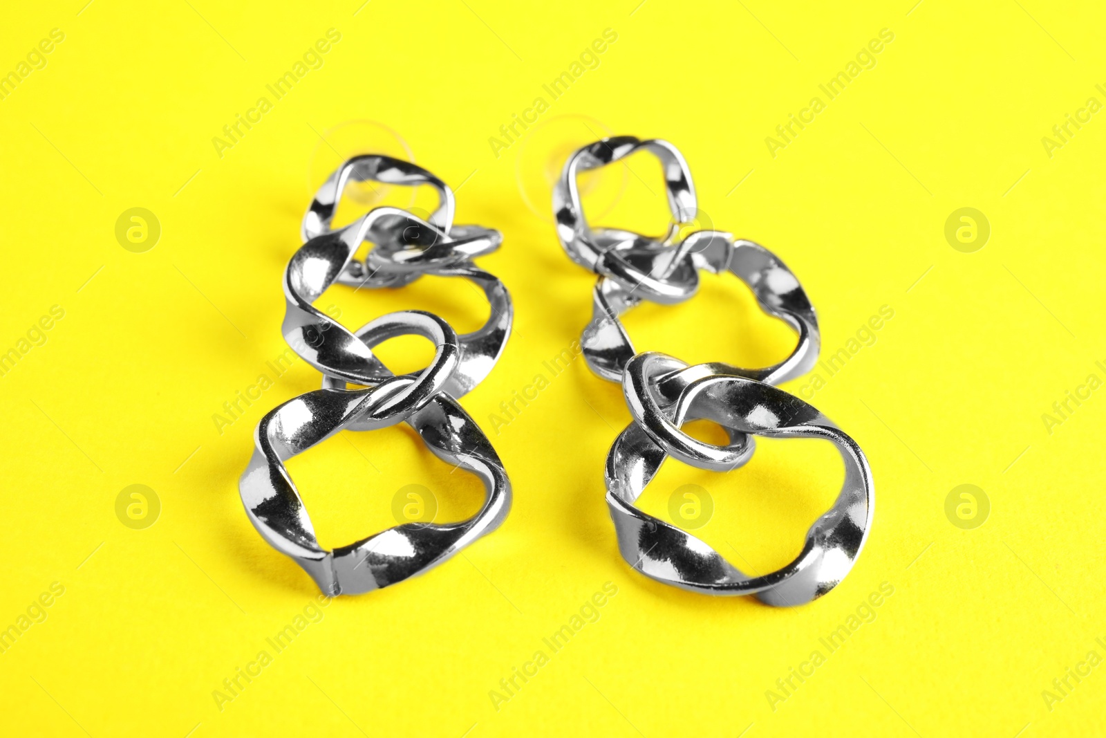 Photo of Beautiful bijouterie. Stylish earrings on yellow background, closeup