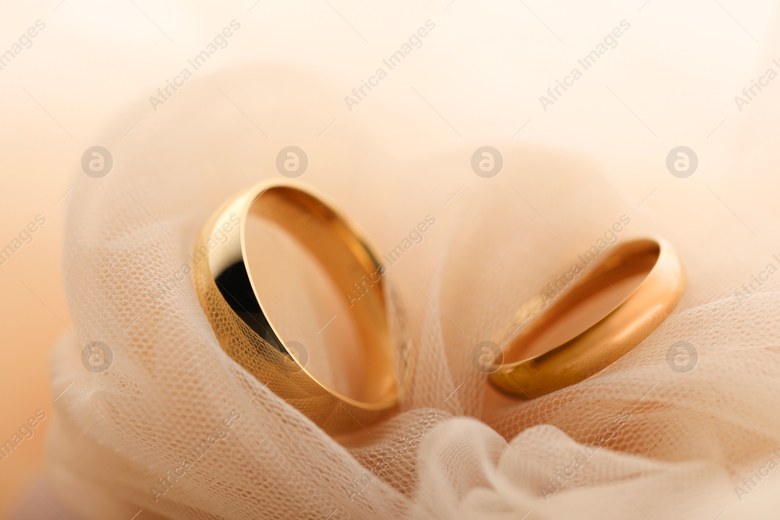 Photo of Beautiful golden wedding rings on beige fabric, closeup