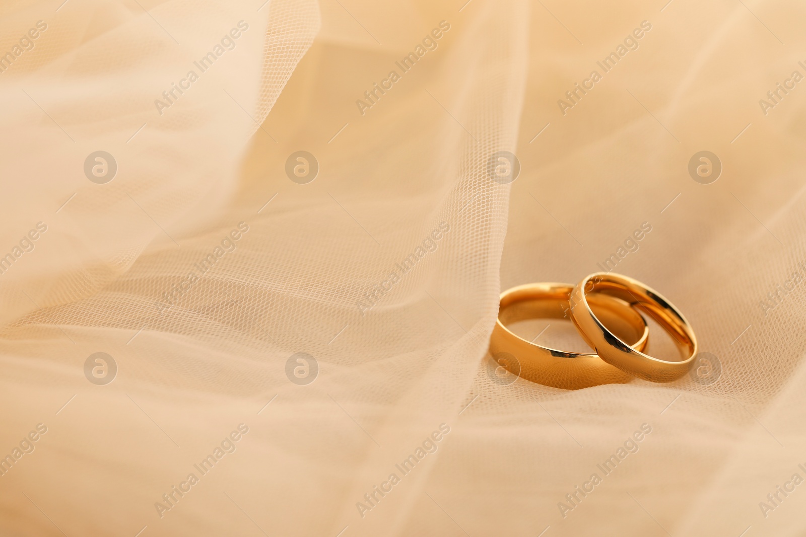 Photo of Beautiful golden wedding rings on beige fabric, space for text