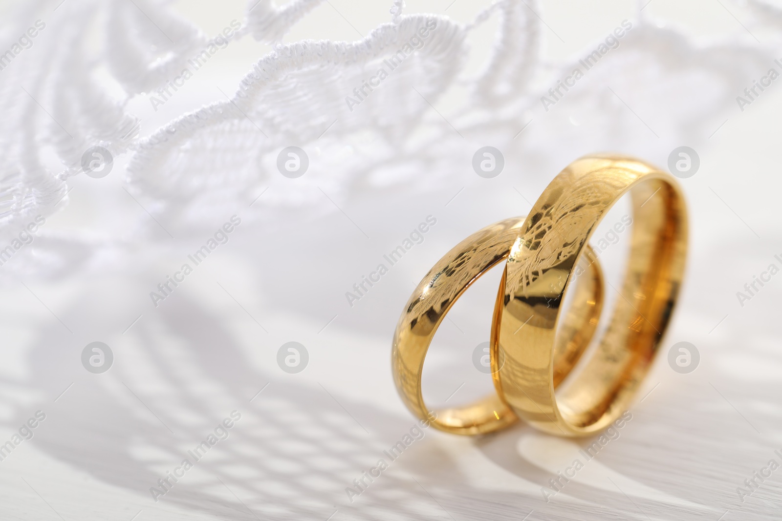 Photo of Beautiful golden wedding rings and white lace on light background