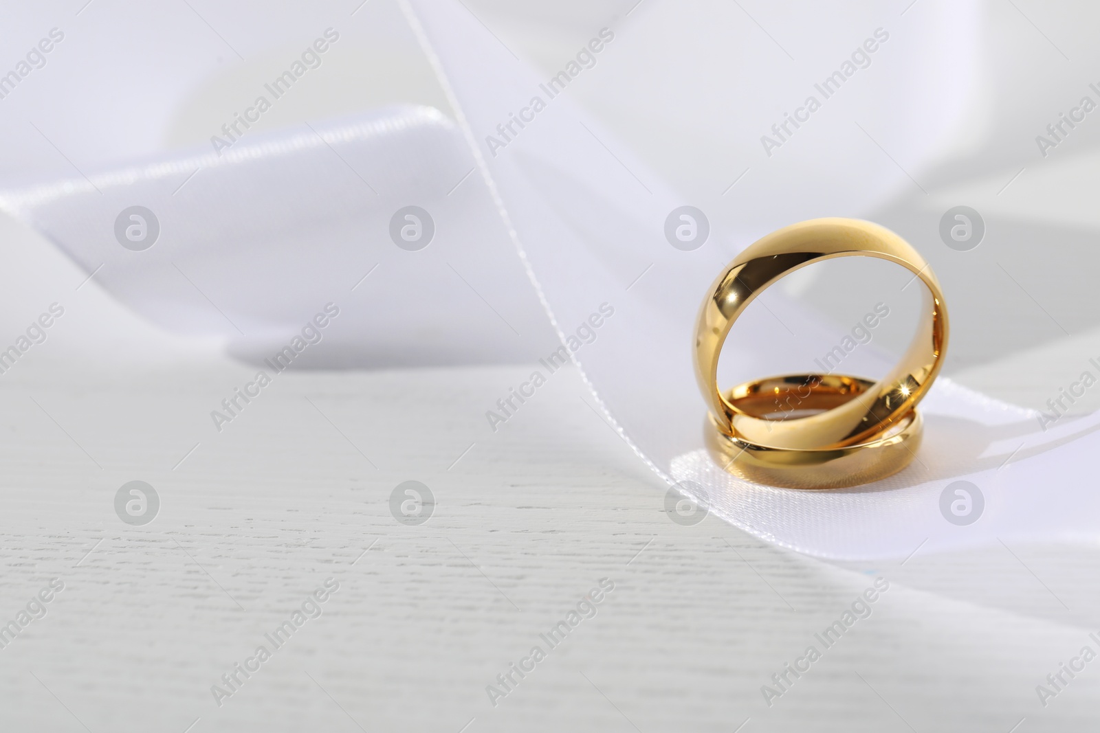 Photo of Beautiful golden wedding rings and white ribbon on light wooden background