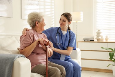 Photo of Caregiver supporting senior woman on sofa. Home health care service