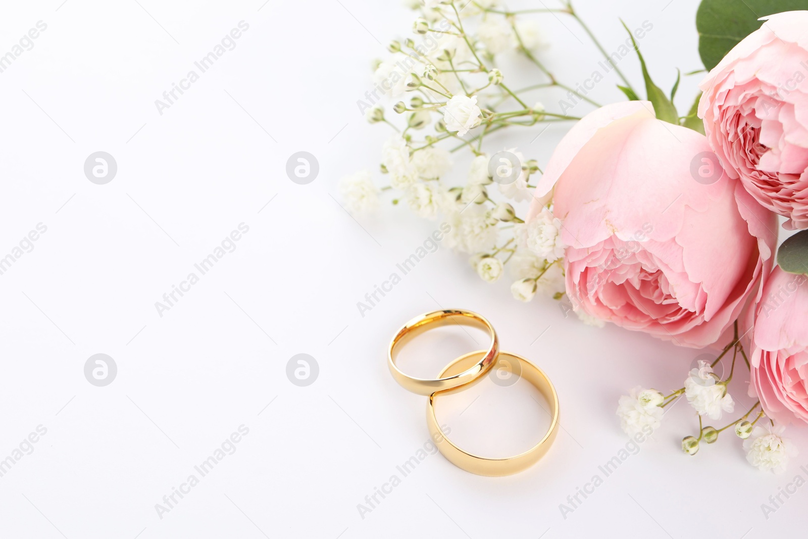 Photo of Golden wedding rings and flowers on white background. Space for text