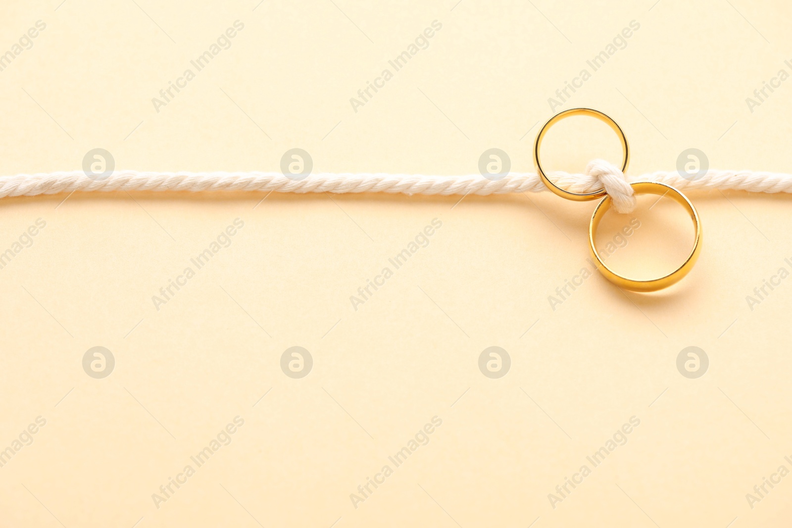 Photo of Golden wedding rings tied with string on beige background, top view