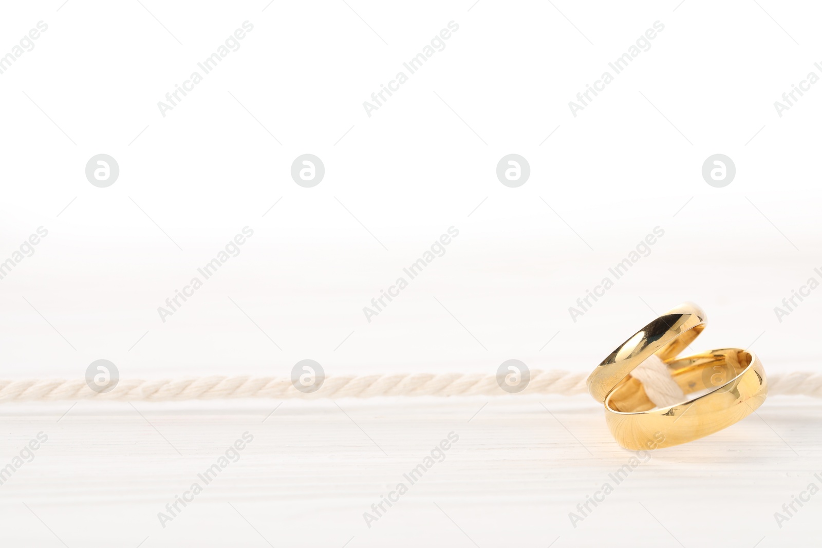 Photo of Golden wedding rings tied with string on white wooden background, closeup. Space for text