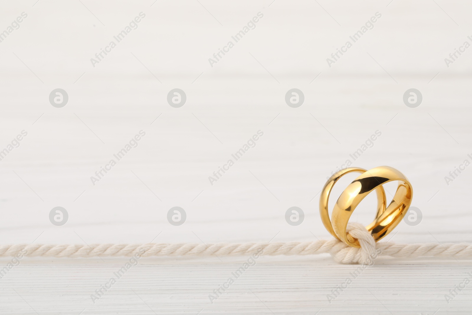 Photo of Golden wedding rings tied with string on white wooden background, closeup. Space for text