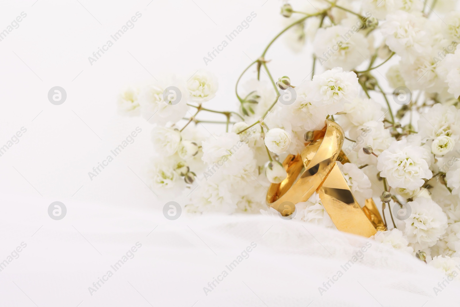 Photo of Golden wedding rings, veil and flowers on blurred background, closeup. Space for text