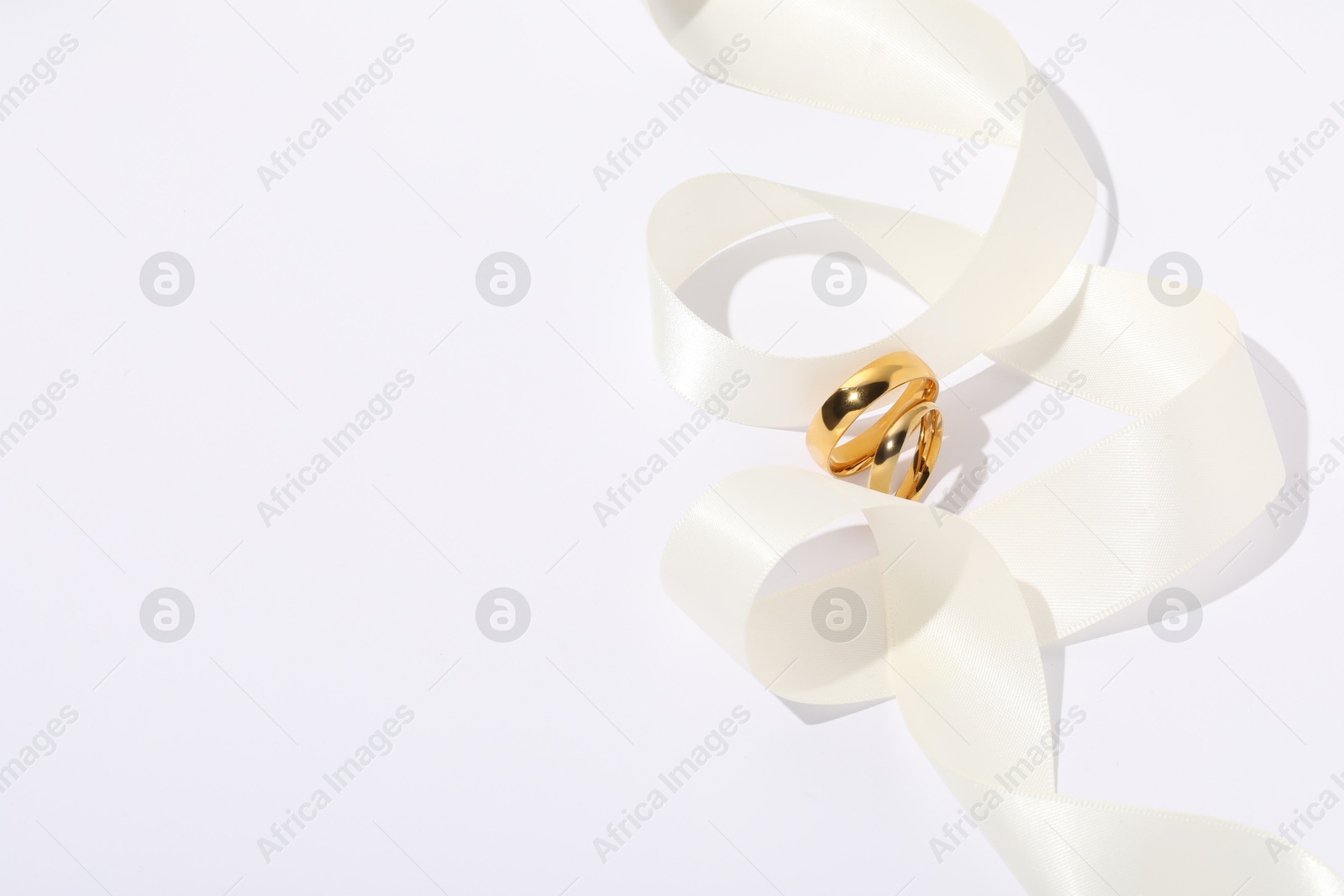 Photo of Golden wedding rings and ribbon on white background, space for text