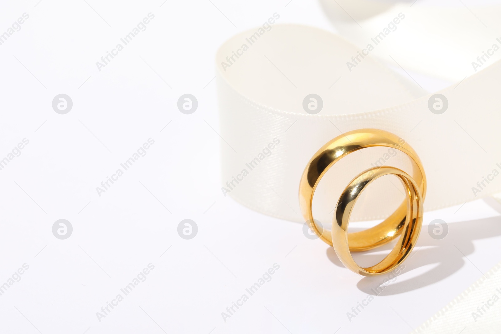 Photo of Golden wedding rings and ribbon on white background, closeup. Space for text