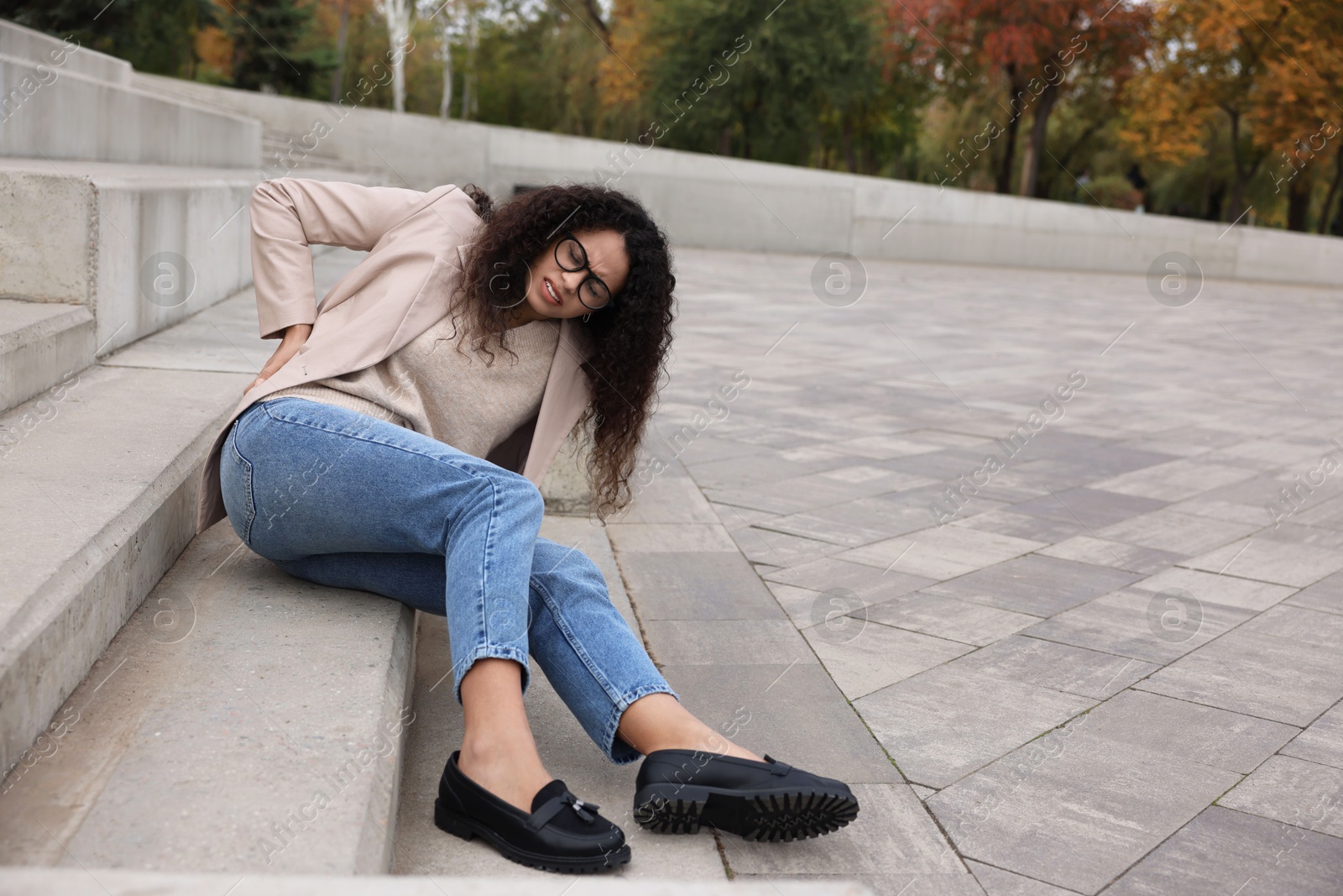 Photo of Woman with injured back on stairs outdoors after fall. Dangerous accident